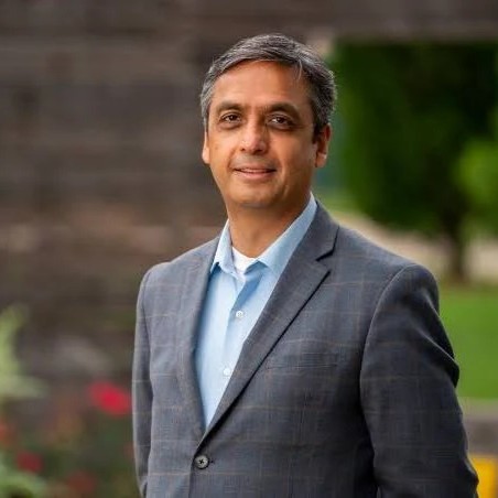 Man in a sport coat posed outside.