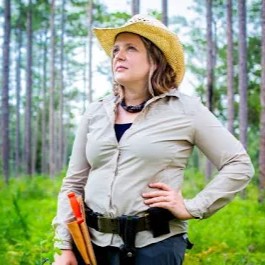 Woman standing hand on hip in a forest wearing a hat and 