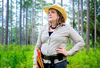 Quave head shot Woman standing hand on hip in a forest wearing a hat and